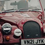 A classic red convertible car with a driver, captured at a car show, showcasing its vintage design.