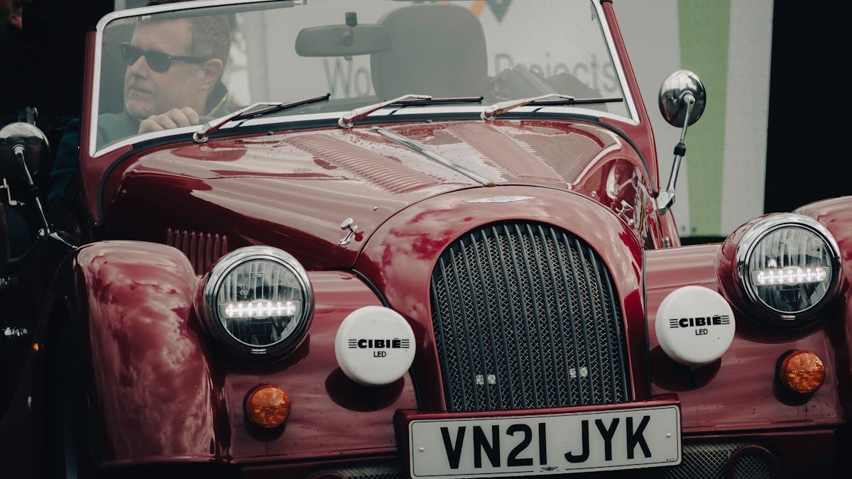 A classic red convertible car with a driver, captured at a car show, showcasing its vintage design.
